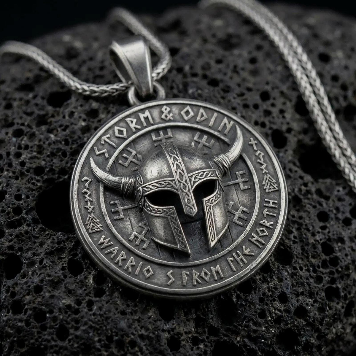 Oxidized sterling silver Viking helmet pendant on black volcanic rock, featuring a horned warrior helmet, Storm and Odin lettering, and Norse-inspired rune symbols.