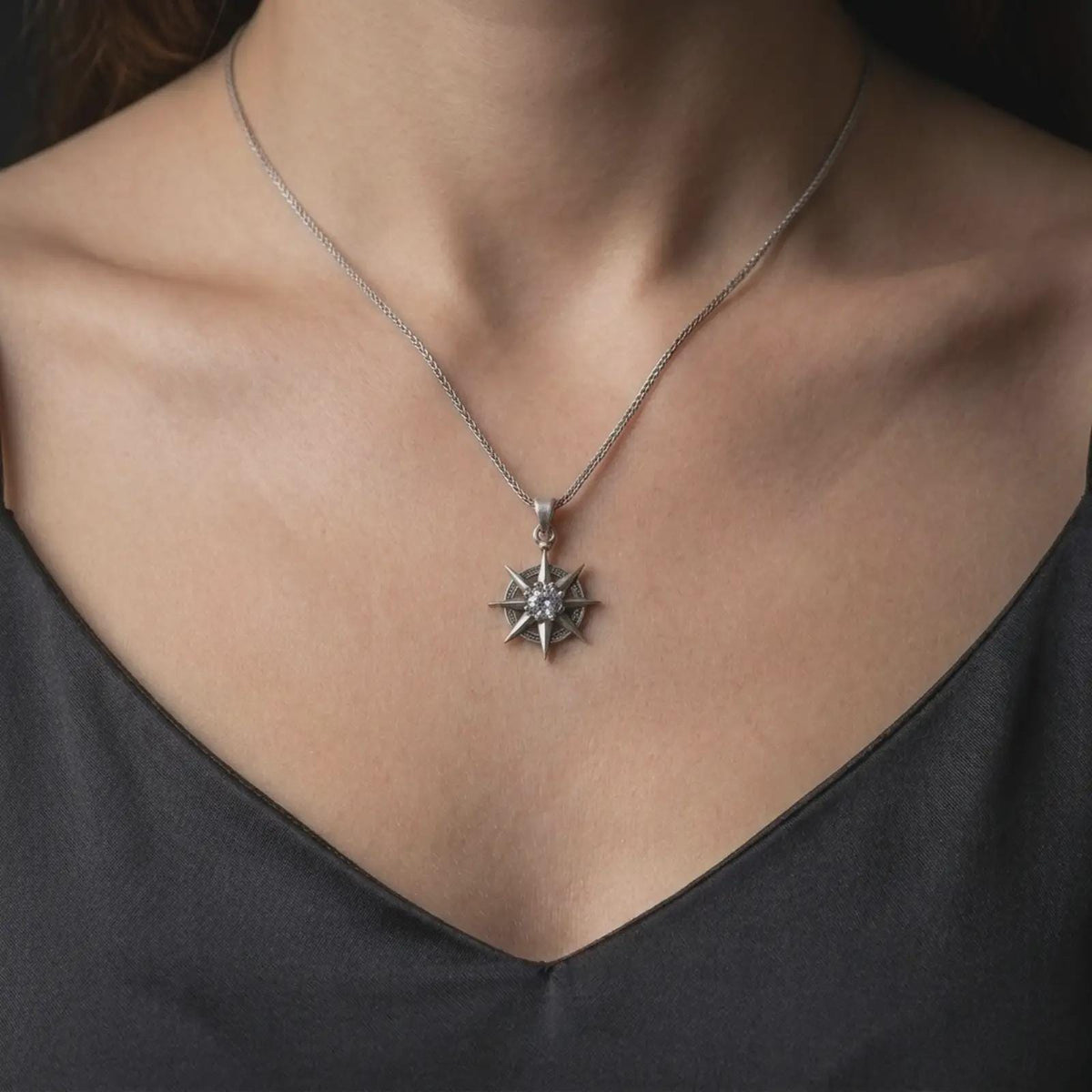 Oxidized sterling silver Gale necklace worn on the chest, showing the eight-point star charm, clear faceted center stone, and distinctive Wizard of Waterdeep inspired design.