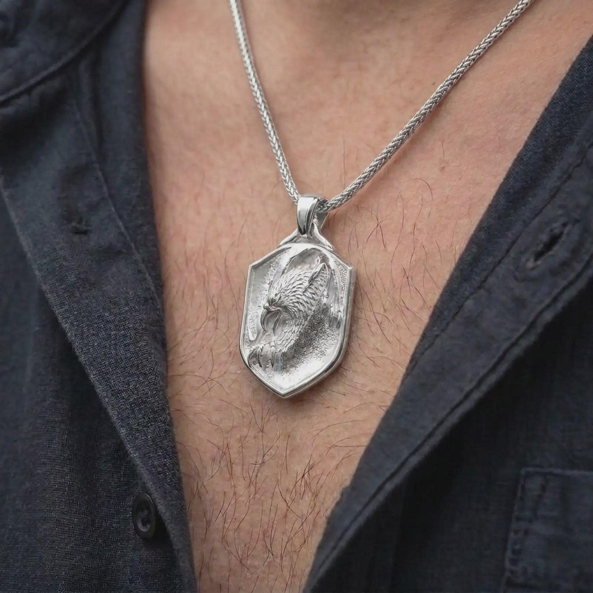 Polished silver eagle shield necklace worn on the chest, featuring sculpted feathers, powerful eagle imagery, claw details, and a bold symbolic pendant design.