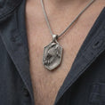 Load image into Gallery viewer, Oxidized sterling silver eagle pendant worn on the chest, showing the detailed bird of prey head, sharp talons, textured background, and masculine shield profile.
