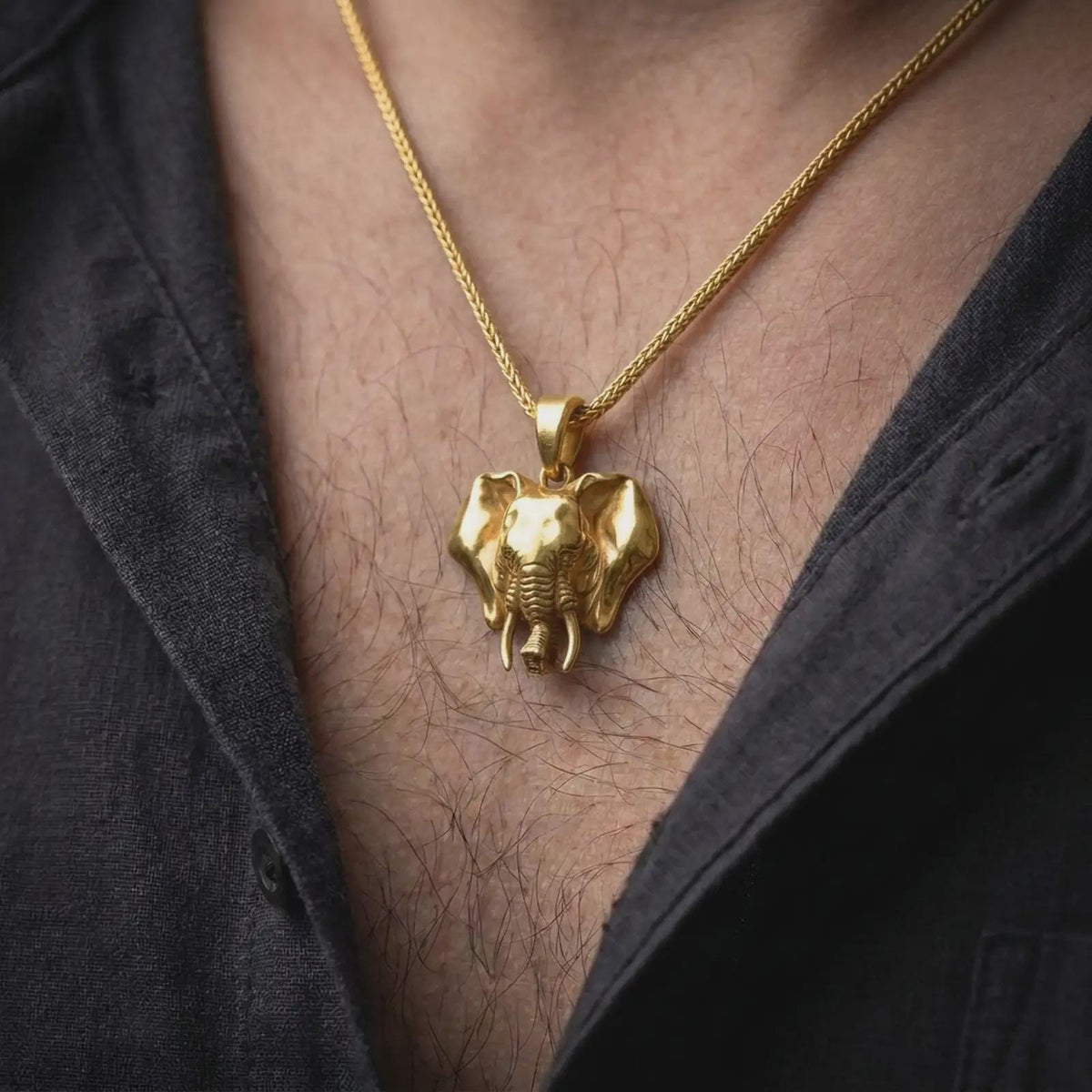 Gold plated elephant necklace worn on the chest, highlighting the detailed elephant head, prominent tusks, dimensional trunk, and powerful wildlife statement jewelry style.