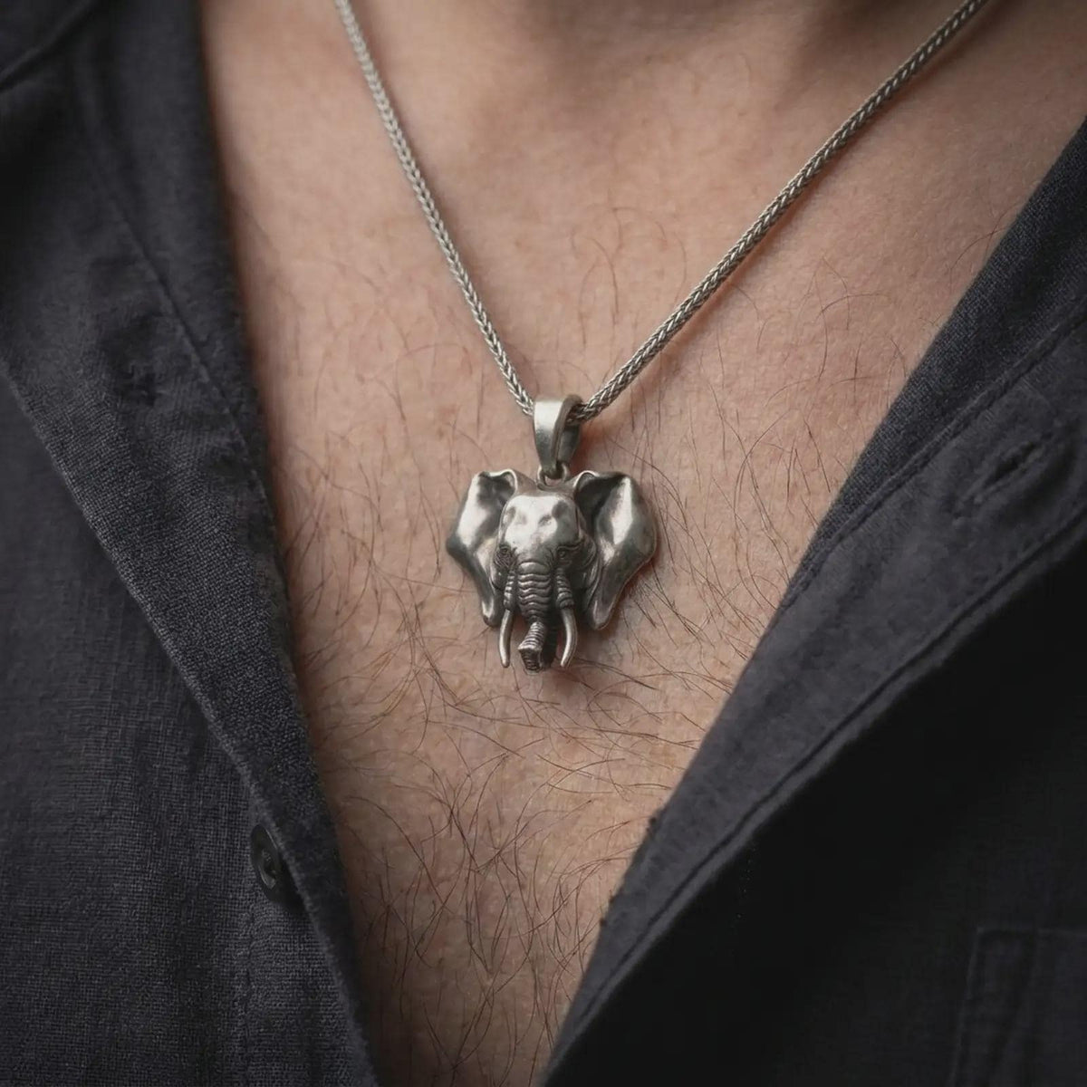 Oxidized sterling silver elephant pendant worn on the chest, showing the realistic animal head, detailed ears, long tusks, and bold three-dimensional wildlife jewelry design.