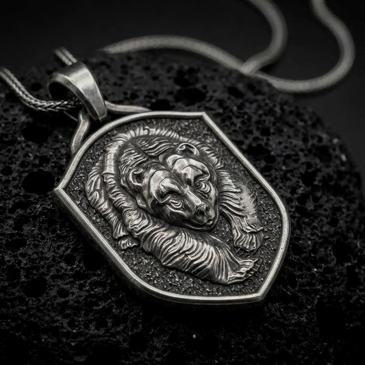 Oxidized sterling silver grizzly bear shield pendant on black volcanic rock, featuring a sculpted bear head, layered fur relief, textured background, and raised shield border.