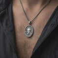 Load image into Gallery viewer, Oxidized sterling silver Padre Pio necklace worn on the chest, showing the sculpted Saint Pio portrait, raised blessing hand, textured oval medallion, and distinctive Catholic faith jewelry design.
