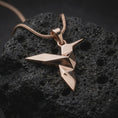 Load image into Gallery viewer, Rose gold plated hummingbird necklace on textured volcanic stone, featuring a folded origami style bird pendant with angular body lines and a minimalist elegant finish.
