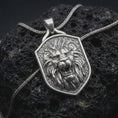 Load image into Gallery viewer, Polished sterling silver lion head necklace displayed on dark volcanic stone, highlighting the roaring lion face, sculpted mane, powerful expression, and detailed shield-shaped medallion.

