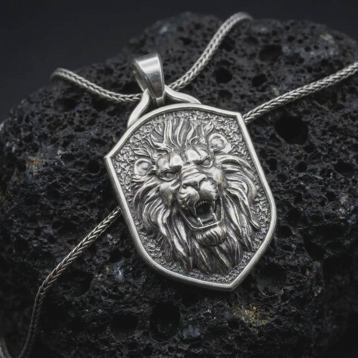 Polished sterling silver lion head necklace displayed on dark volcanic stone, highlighting the roaring lion face, sculpted mane, powerful expression, and detailed shield-shaped medallion.