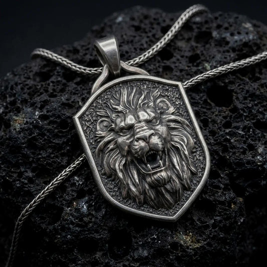 Oxidized sterling silver roaring lion shield pendant on black volcanic rock, featuring a fierce lion head, open jaws, sharp fangs, flowing mane, and textured heraldic shield background.