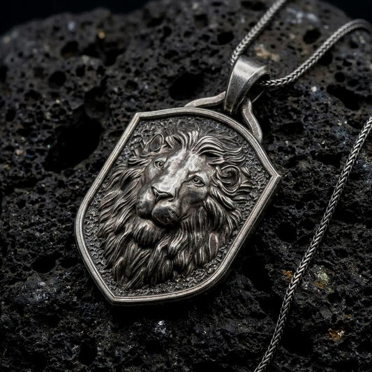 Oxidized sterling silver regal lion shield pendant on black volcanic rock, featuring a majestic lion portrait, calm expression, flowing mane, and textured heraldic shield background.