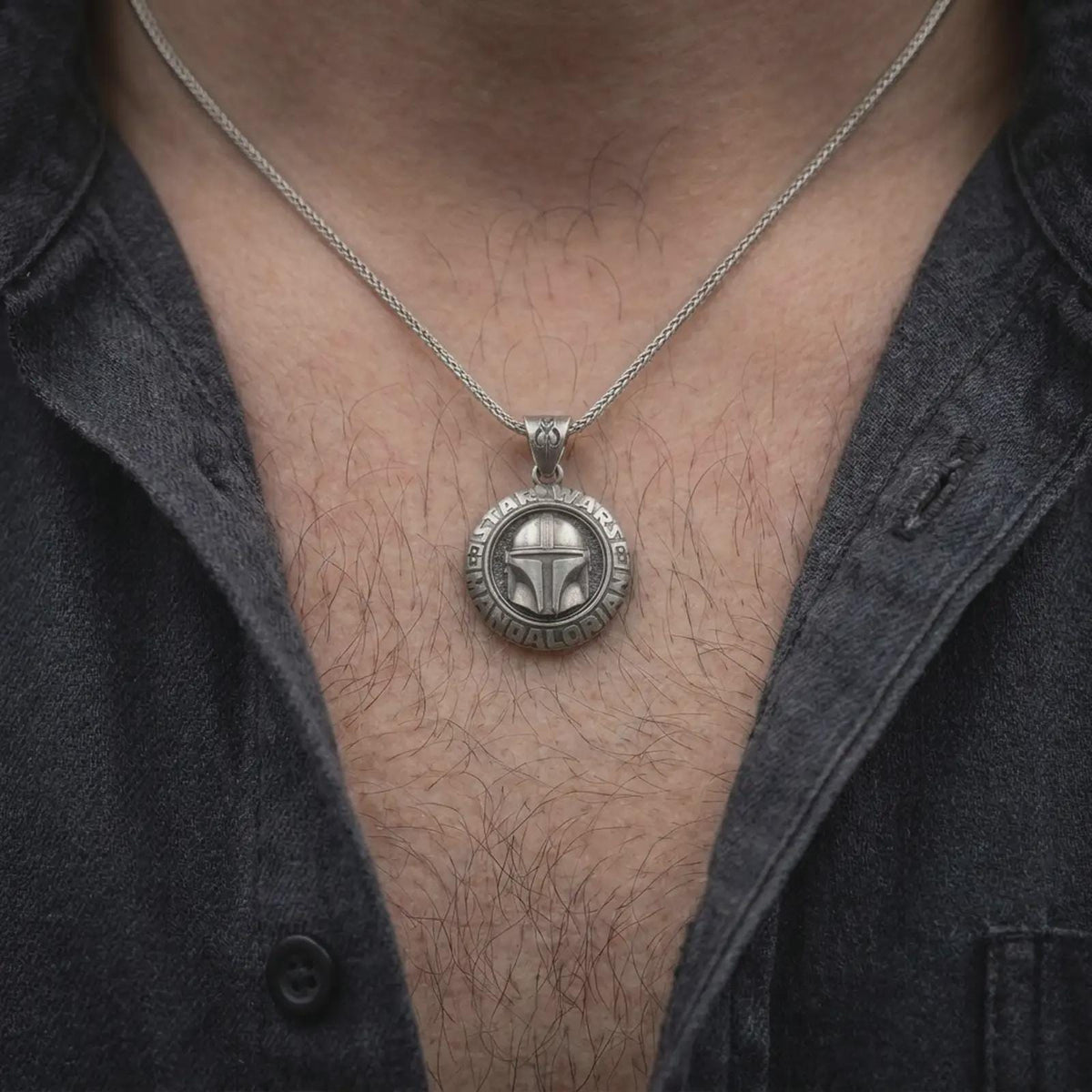 Oxidized sterling silver Mandalorian helmet necklace worn on the chest, showing the detailed bounty hunter mask, circular Star Wars medallion, and bold sci-fi inspired pendant design.