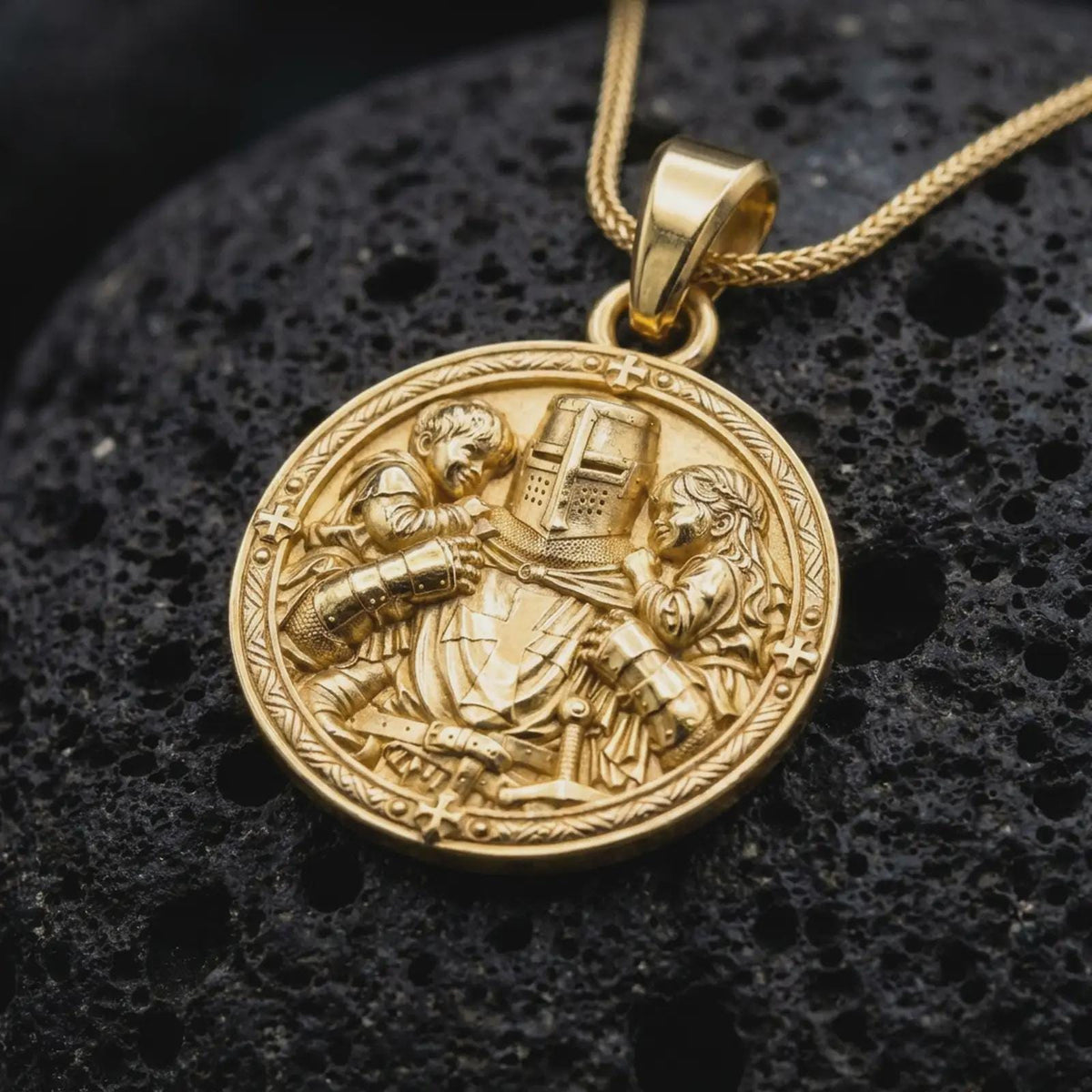 Gold plated medieval knight pendant resting on black volcanic rock, featuring a protective armored warrior with two children, cross-adorned great helm, and detailed round medallion design.