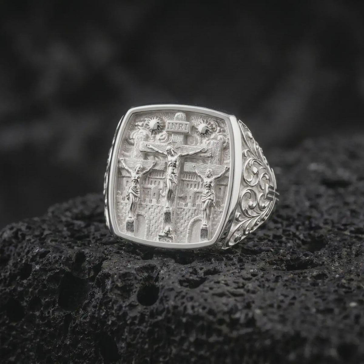 Polished sterling silver Jesus and two thieves ring displayed on dark volcanic stone, highlighting the three crosses, Christ figure, Jerusalem architecture, and detailed Christian signet design.