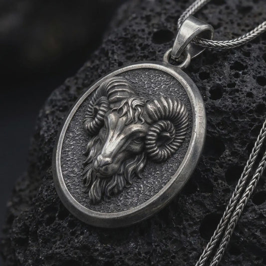 Oxidized sterling silver Aries ram pendant on black volcanic rock, featuring a sculpted ram head, large curled horns, textured background, and oval medallion frame.