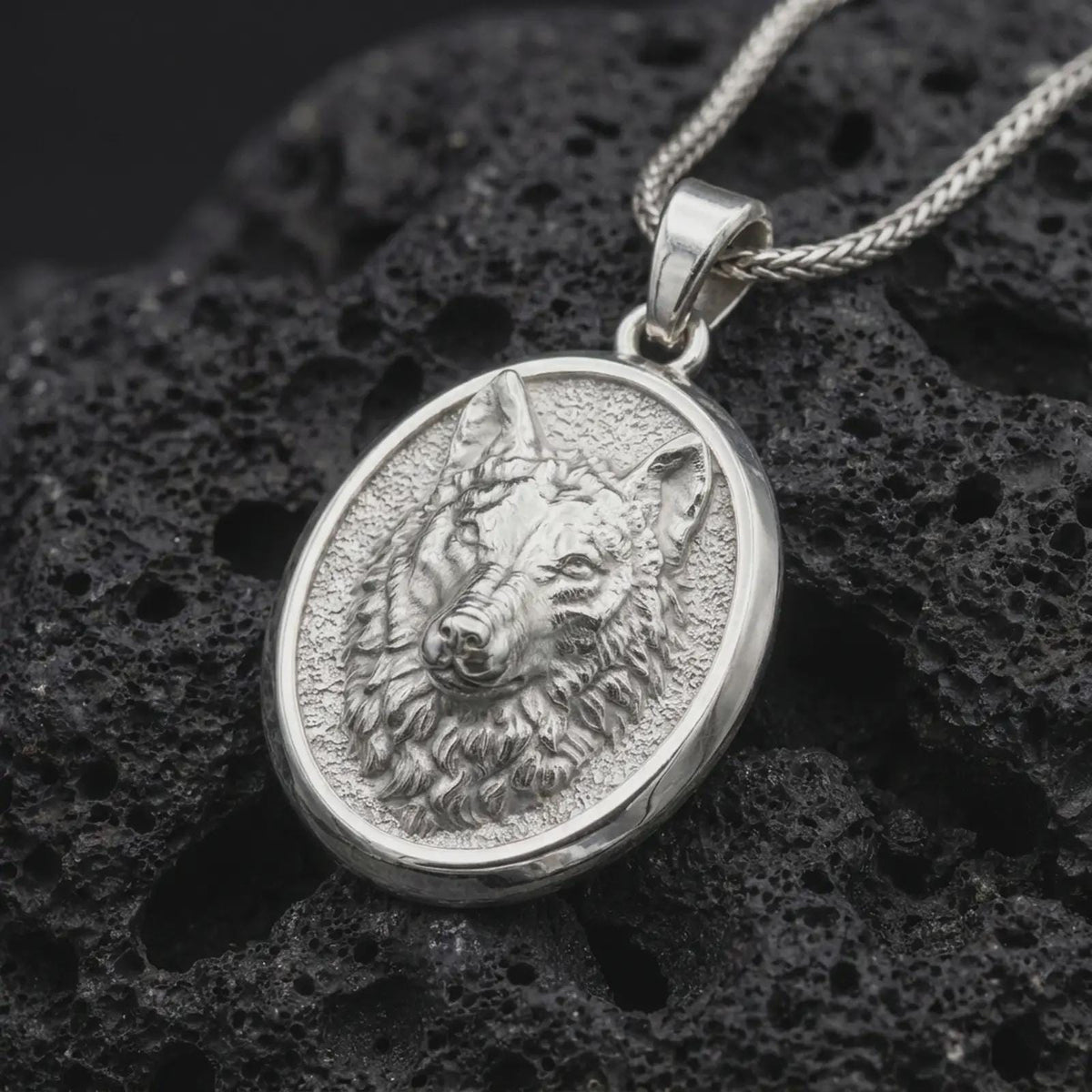 Polished sterling silver wolf necklace displayed on dark volcanic stone, highlighting the realistic wolf portrait, layered fur details, alert ears, and oval animal medallion.