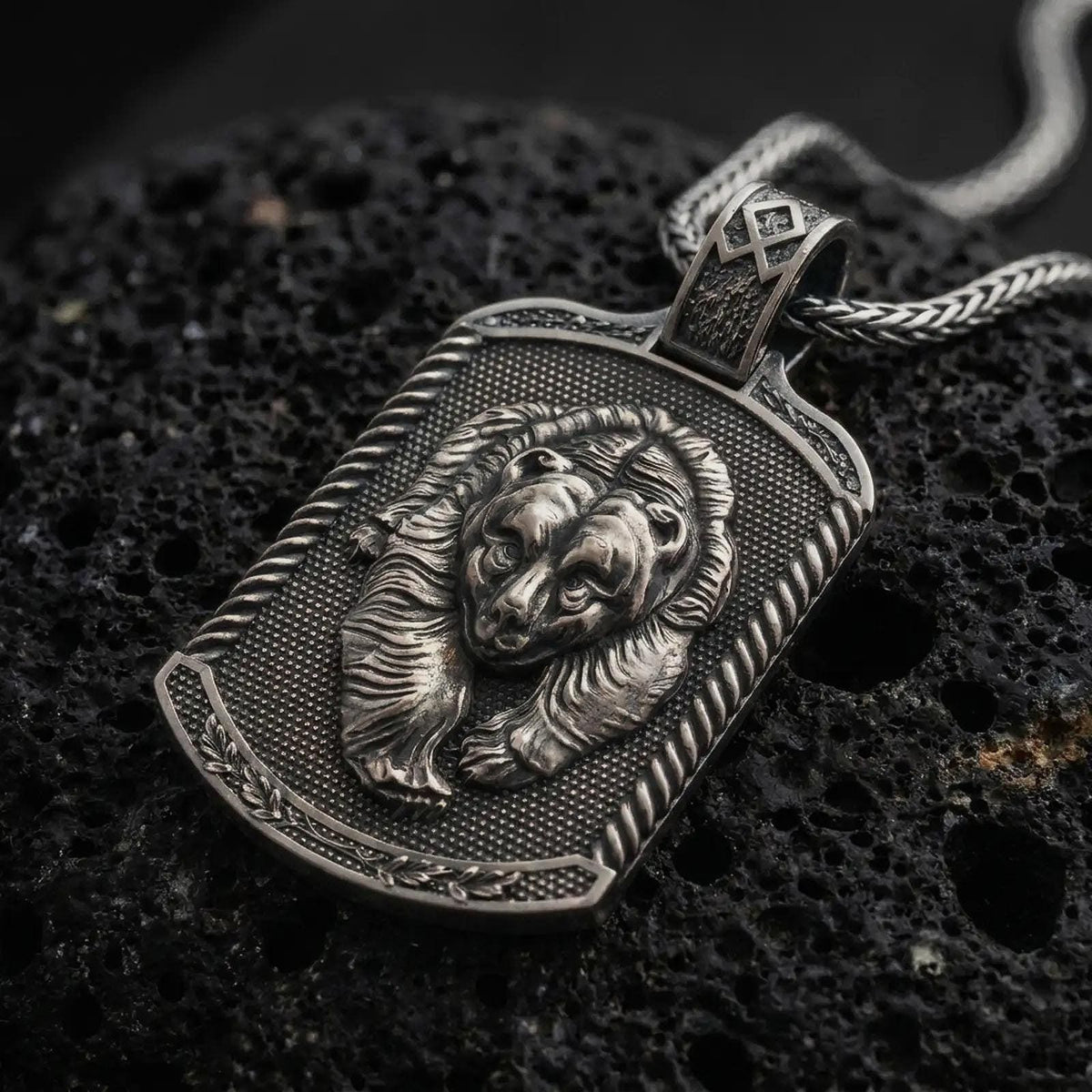 Oxidized sterling silver bear and cub pendant on black volcanic rock, featuring two sculpted bear faces, detailed fur, textured dog tag background, and decorative border.