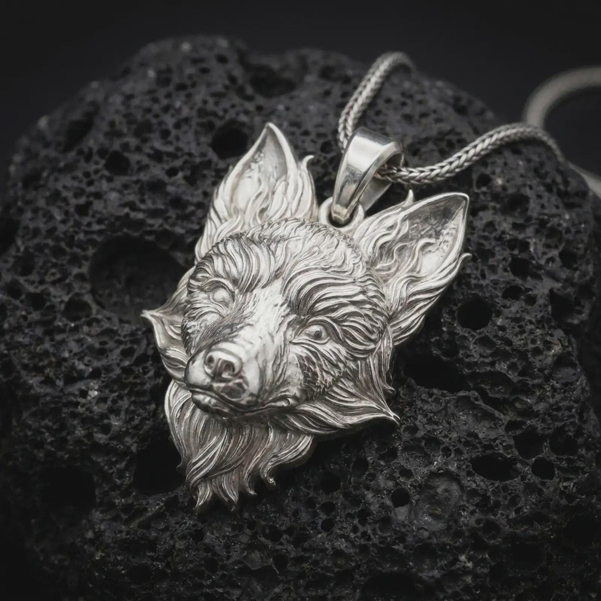 Polished sterling silver fox necklace displayed on dark volcanic stone, highlighting the realistic fox face, upright ears, layered fur details, and dimensional animal design.