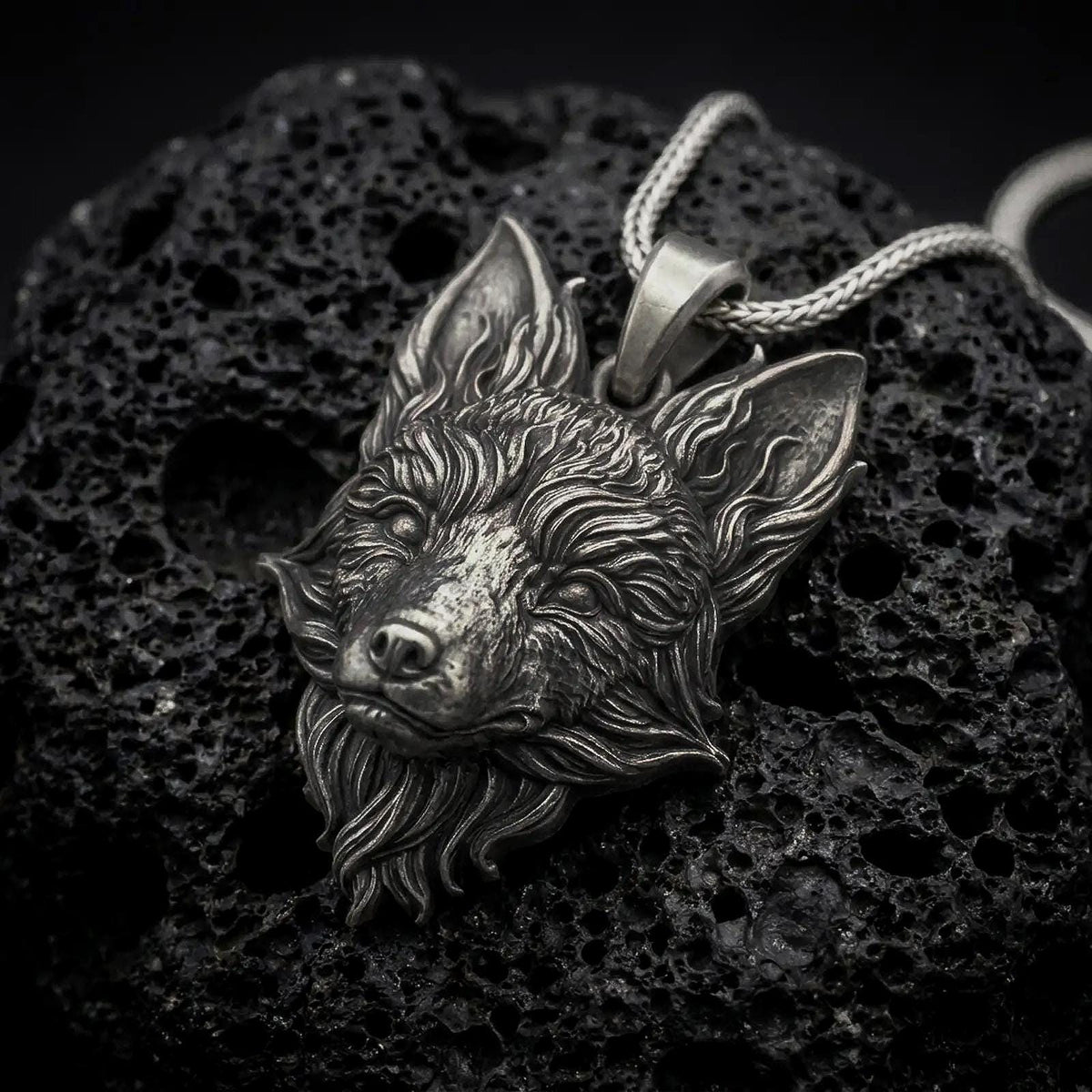 Oxidized sterling silver fox head pendant on black volcanic rock, featuring pointed ears, a narrow sculpted muzzle, expressive eyes, and detailed flowing fur.