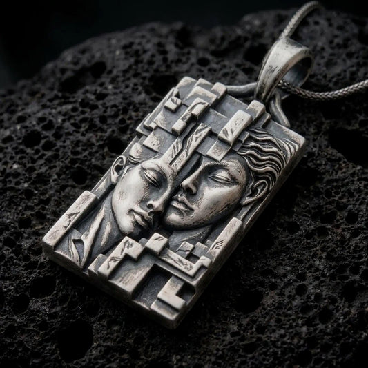 Oxidized sterling silver Gemini twins pendant on black volcanic rock, featuring two sculpted faces resting together, detailed facial expressions, and an intricate geometric rectangular frame.