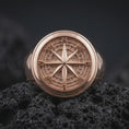 Load image into Gallery viewer, Rose gold plated compass signet ring displayed on textured volcanic stone, showcasing the raised compass rose centerpiece, engraved navigation dial, recessed directional markings, and smooth rounded band.
