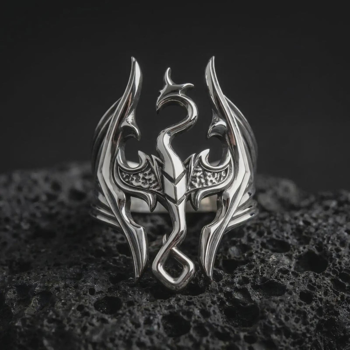 Polished sterling silver Elder Scrolls dragon ring displayed on dark volcanic stone, highlighting the sculpted Imperial Dragon crest, sharply pointed wings, curved tail, and intricate three-dimensional silver detailing.