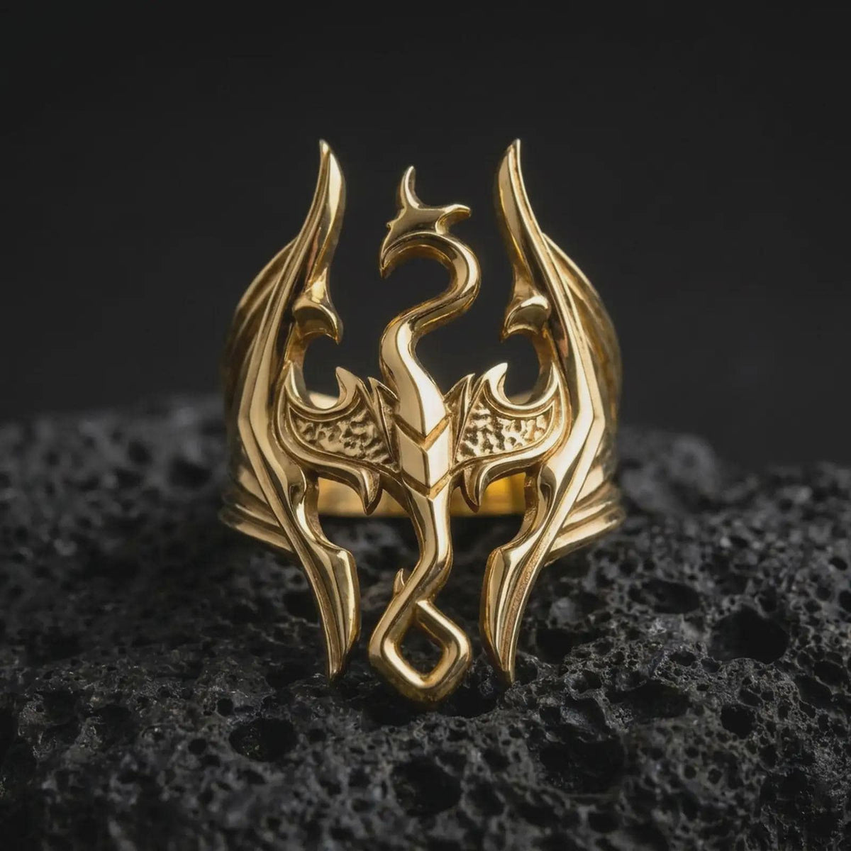 Gold plated Skyrim-inspired Dragonborn ring resting on black volcanic rock, featuring the legendary dragon emblem, symmetrical angular wings, curled serpentine body, and distinctive openwork fantasy jewelry design.
