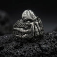 Load image into Gallery viewer, Oxidized sterling silver Cthulhu ring on black volcanic rock, featuring a monstrous Lovecraftian face, deeply recessed eyes, thick facial tentacles, and detailed octopus suction cups.
