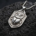 Load image into Gallery viewer, Polished sterling silver stag beetle necklace displayed on dark volcanic stone, highlighting the three-dimensional beetle body, curved mandibles, segmented wing covers, and shield-shaped medallion frame.
