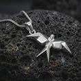 Load image into Gallery viewer, Polished sterling silver swallow necklace displayed on dark volcanic stone, highlighting the angular origami wings, folded geometric body, and modern bird design.
