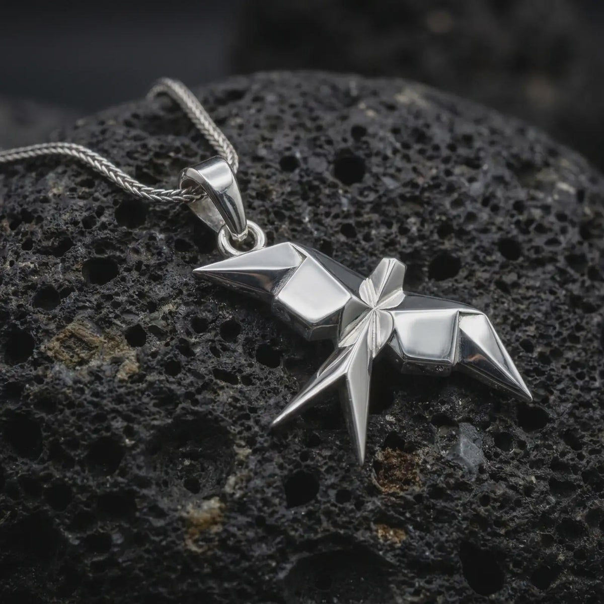 Polished sterling silver swallow necklace displayed on dark volcanic stone, highlighting the angular origami wings, folded geometric body, and modern bird design.