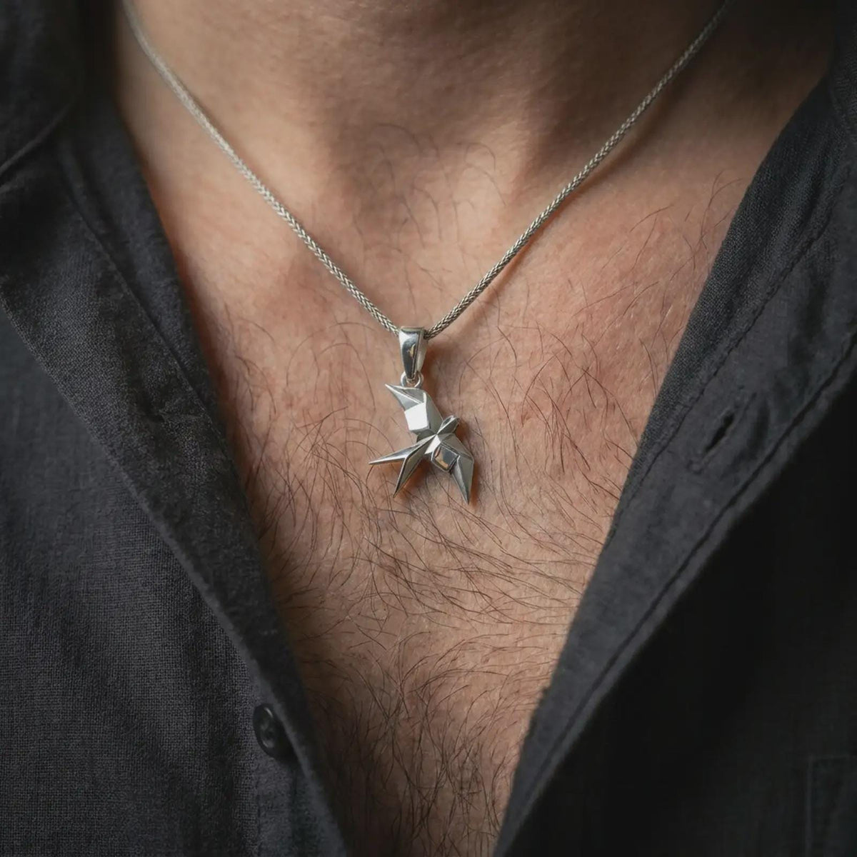 Polished silver origami swallow pendant worn on the chest, featuring sharp faceted surfaces, swept wings, and modern minimalist bird jewelry styling.