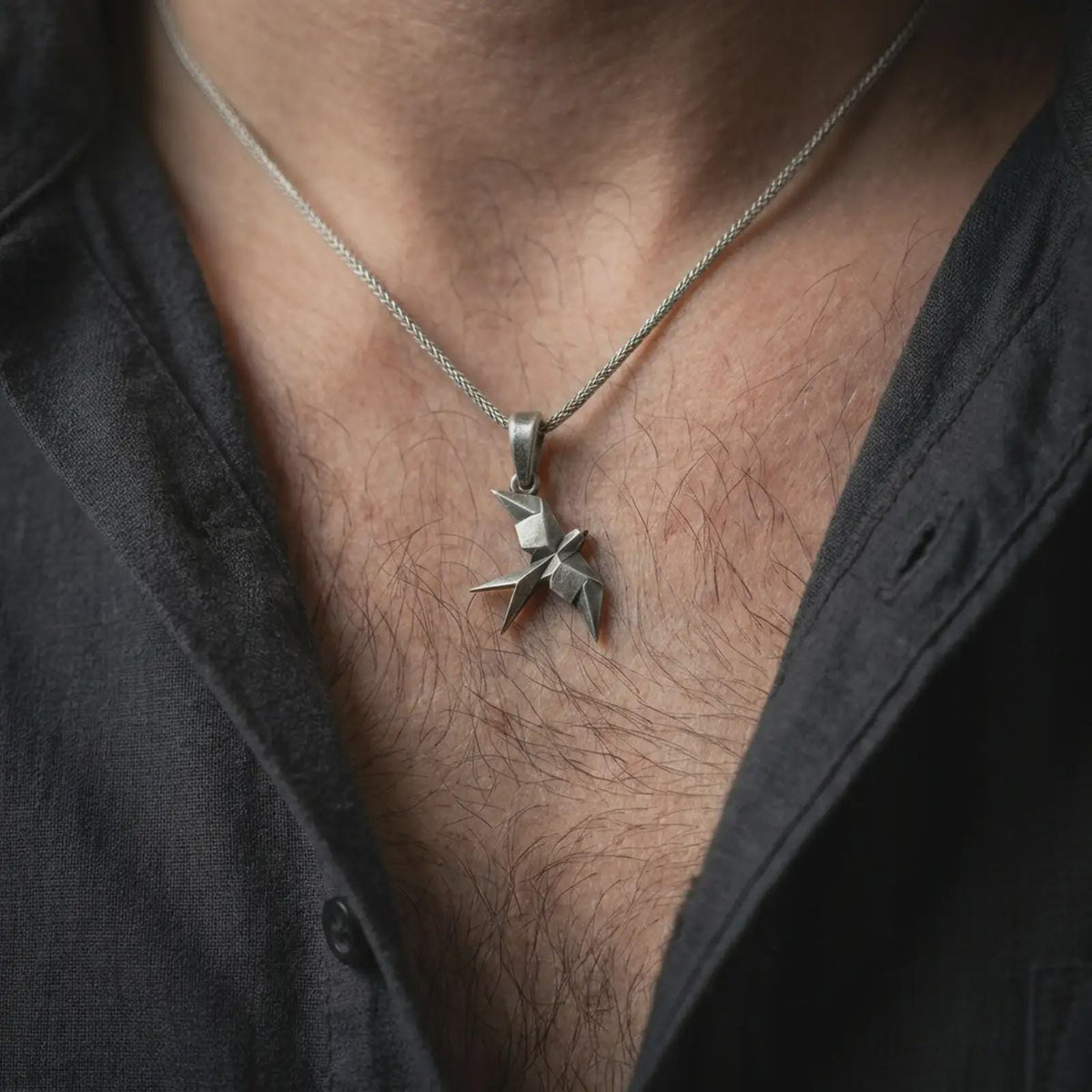 Oxidized sterling silver swallow necklace worn on the chest, showing the geometric flying bird silhouette, pointed wings, and distinctive origami pendant shape.