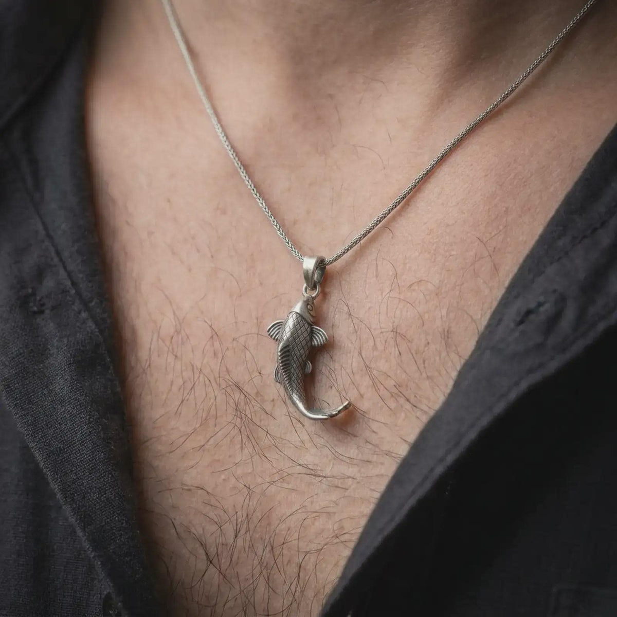 Oxidized sterling silver koi fish necklace worn on the chest, showing the detailed scales, curved swimming form, flowing fins, and symbolic Japanese carp design.