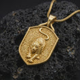 Load image into Gallery viewer, Gold plated leopard necklace resting on black volcanic stone, featuring a sculpted leopard in a stalking pose with intricate spots, powerful paws, curled tail, and a textured wildlife medallion design.
