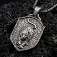 Load image into Gallery viewer, Oxidized sterling silver leopard pendant necklace on black volcanic stone, featuring a prowling spotted leopard with extended front paws, curved tail, textured shield-shaped background, and braided silver chain.

