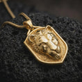 Load image into Gallery viewer, Gold plated lioness necklace resting on black textured stone, featuring a three-dimensional female lion head, powerful expression, detailed nose and whisker area, and a distinctive shield-shaped pendant design.
