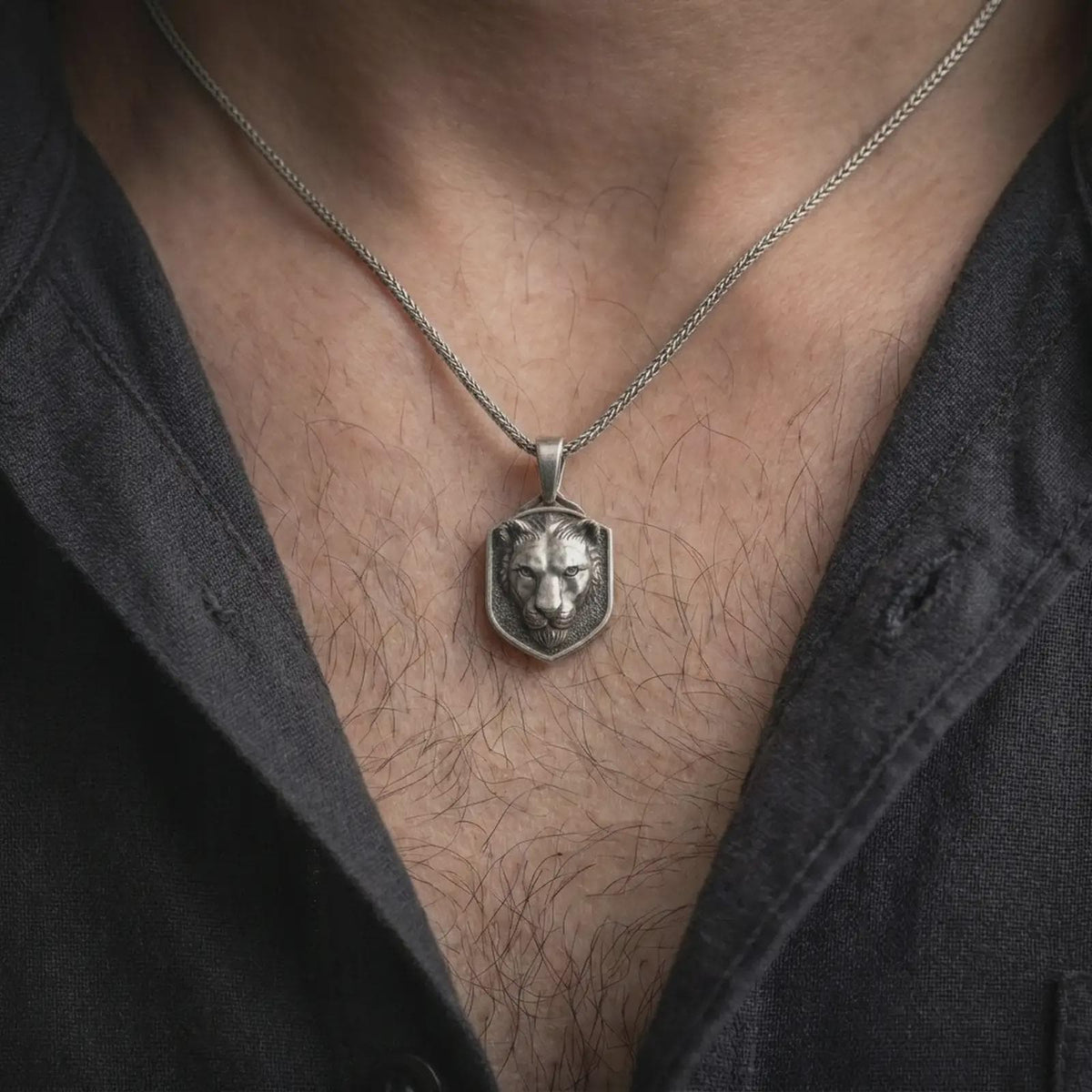 Oxidized sterling silver lioness pendant worn around the neck, showing the raised female lion portrait, strong facial structure, dark textured shield-shaped face, and braided silver necklace chain.