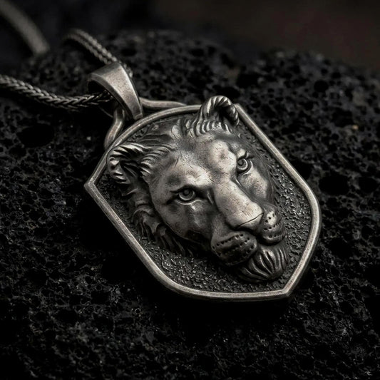 Oxidized sterling silver lioness pendant necklace on black volcanic stone, featuring a raised female lion head with detailed facial contours, textured background, shield-shaped frame, and braided silver chain.
