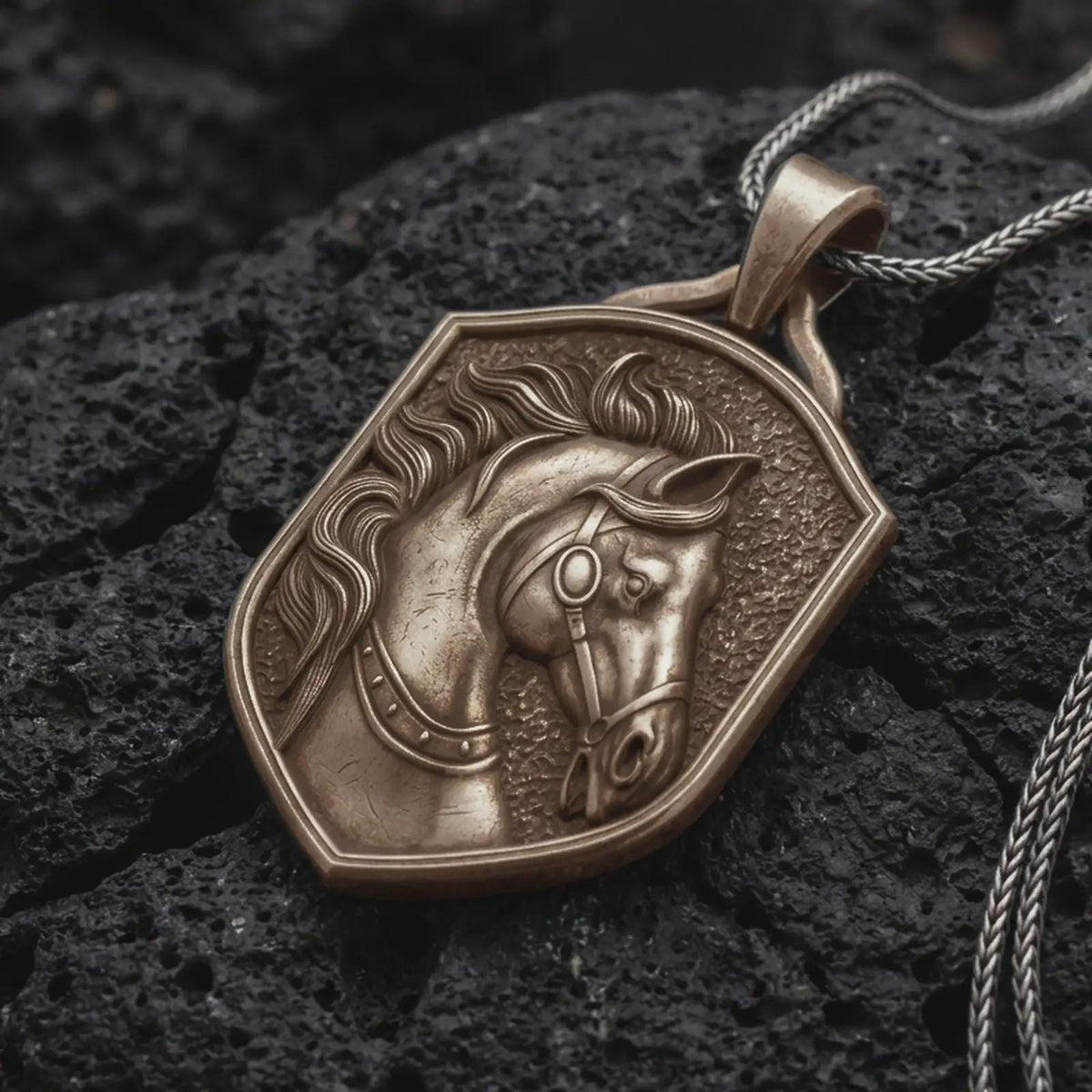 Bronze horse head pendant necklace resting on black volcanic stone, featuring a sculpted horse with a flowing mane, detailed leather-style bridle, expressive eyes, and a textured shield-shaped silver frame.