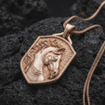 Load image into Gallery viewer, Rose gold plated horse pendant displayed on dark volcanic stone, showcasing the detailed horse head with expressive eyes, flowing sculpted mane, decorative riding bridle, and textured shield-shaped centerpiece.
