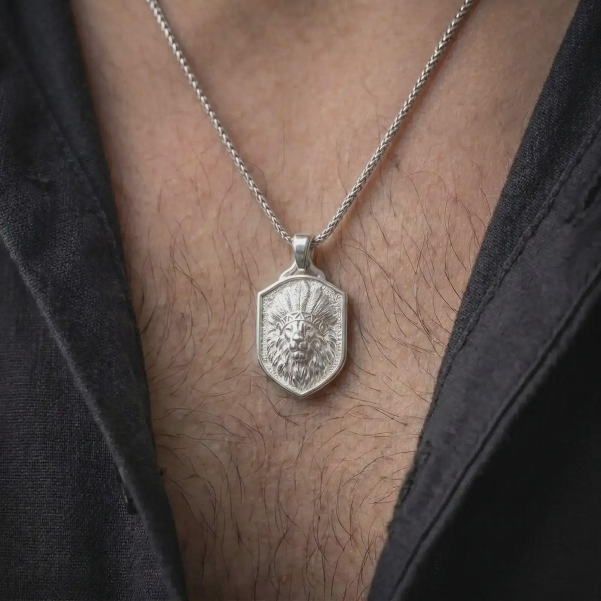 Polished silver feather headdress lion necklace worn on the chest, featuring the dimensional lion head sculpture, detailed layered feathers, powerful facial expression, substantial silver pendant bail, and shield-shaped centerpiece.