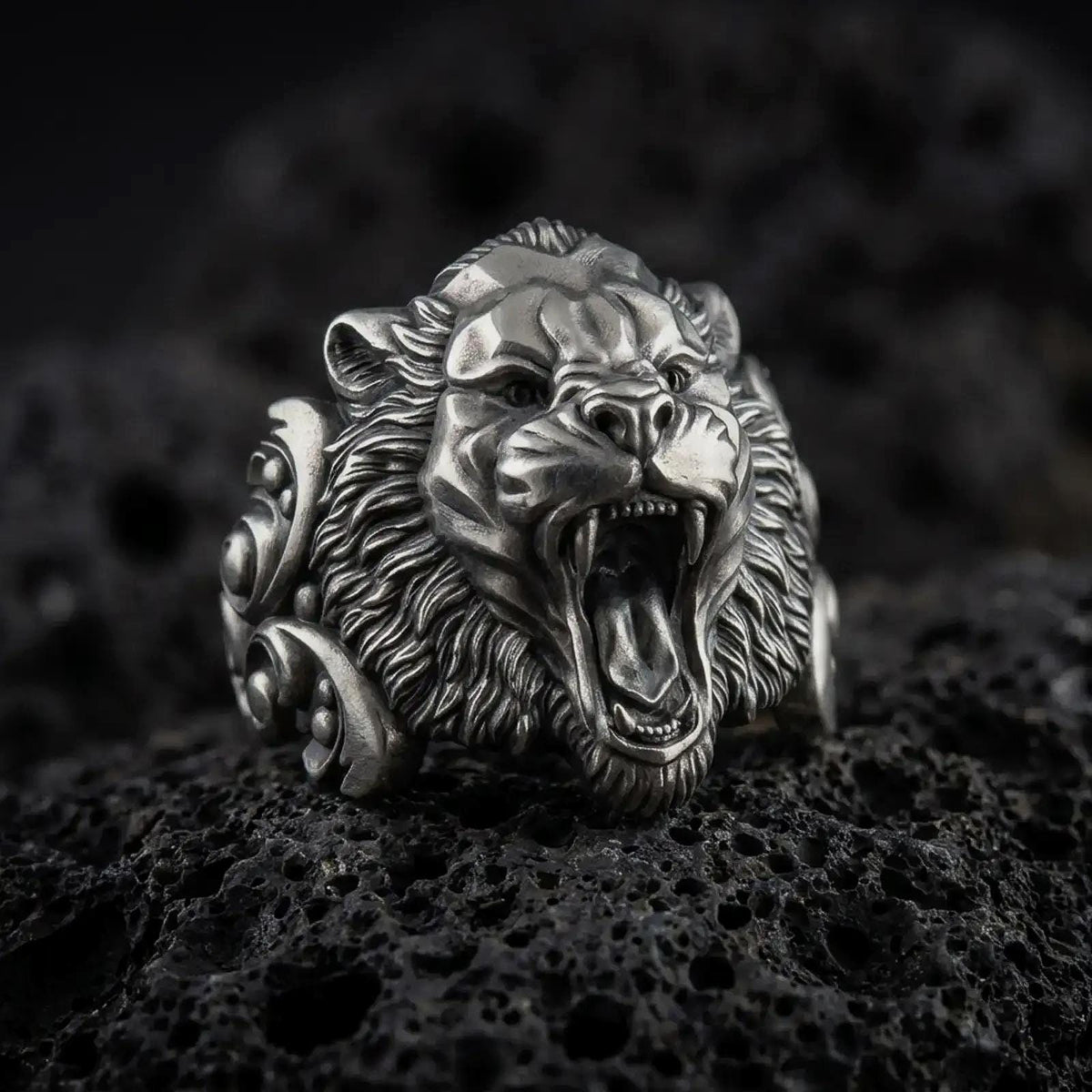 Oxidized sterling silver roaring tiger ring displayed on black volcanic stone, featuring an open mouth, sharp fangs, detailed fur texture, and bold sculptural side accents.