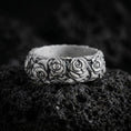 Load image into Gallery viewer, Oxidized 925 sterling silver rose flower band ring displayed on black volcanic rock, featuring three-dimensional rose blossoms, layered petals, sculpted leaves, dark recessed floral details, and a wide ornamental band.

