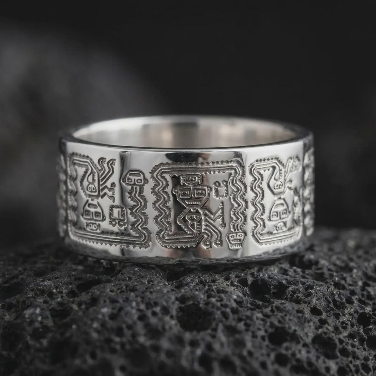 Polished 925 sterling silver Aztec Mayan wedding band resting on black volcanic stone, showcasing detailed ancient-inspired symbols, stylized human figures, repeating zigzag borders, and a bright polished silver finish.