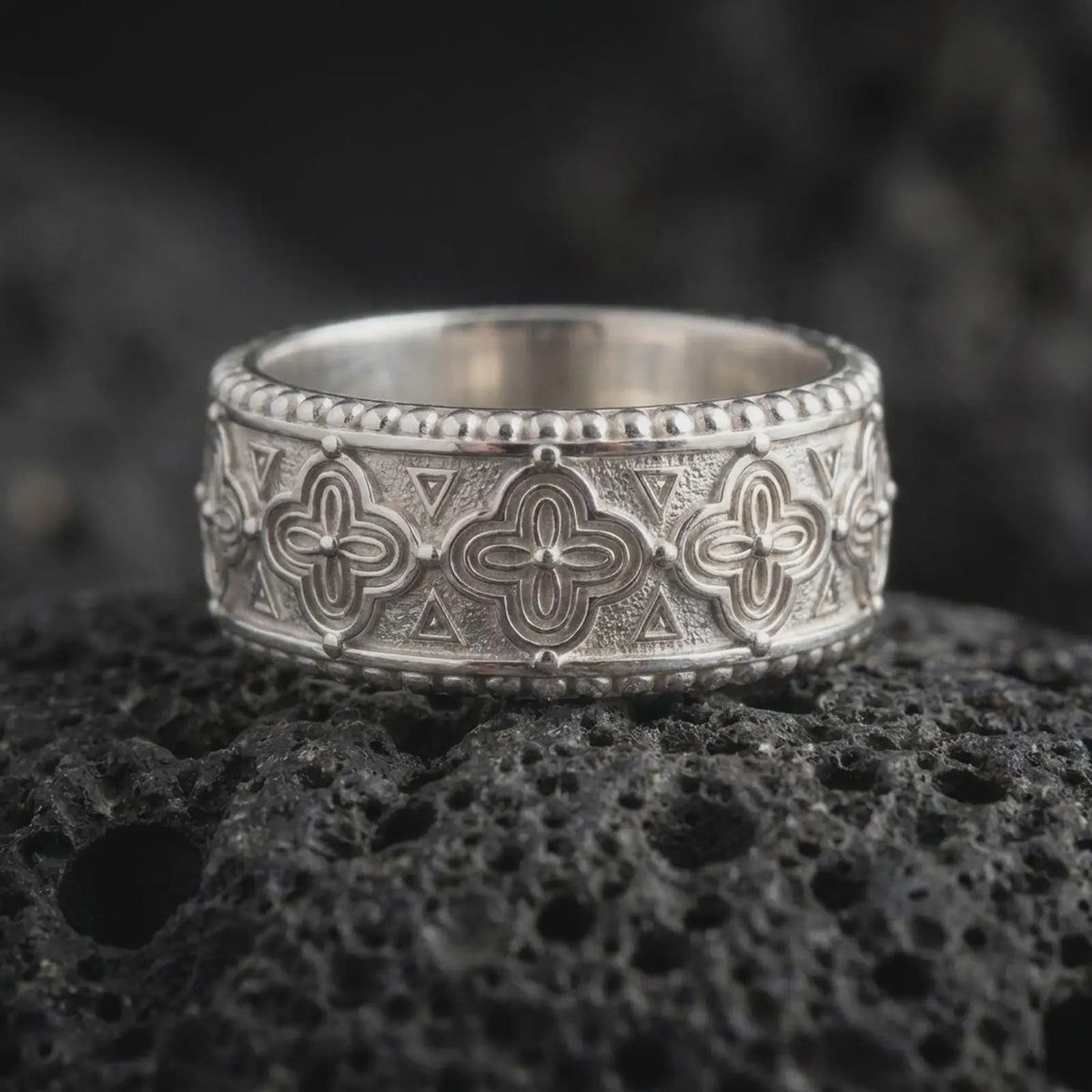 Polished 925 sterling silver Valknut ring resting on black volcanic stone, showcasing repeating triangular Norse motifs, intricate geometric metalwork, textured background, and a bright polished silver finish.