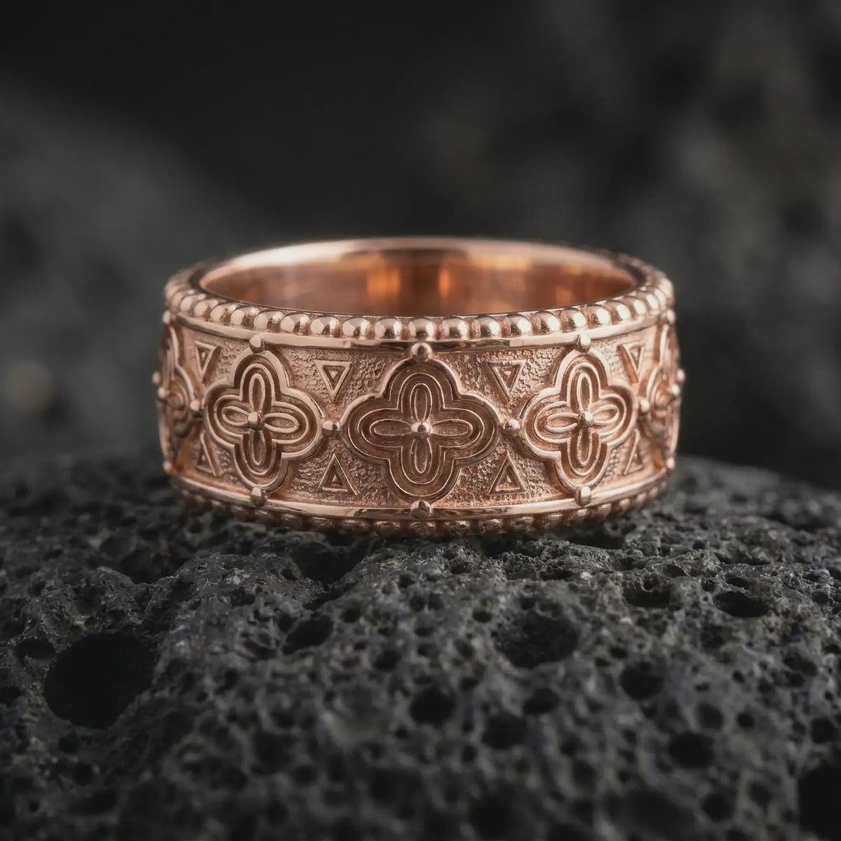 Rose gold plated 925 sterling silver Norse Valknut band resting on black volcanic stone, highlighting repeating triangular symbols, geometric engravings, textured recesses, and a warm rose gold finish.