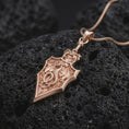 Load image into Gallery viewer, Rose gold plated 925 sterling silver fantasy dragon sword necklace resting on black volcanic stone, highlighting the mythical winged dragon, textured reptilian scales, curling tail, detailed sword hilt, angular blade, and warm rose gold plated finish.
