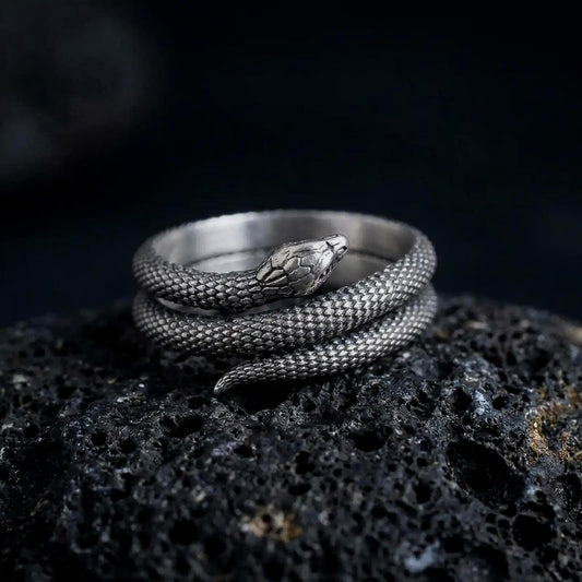 Oxidized 925 sterling silver snake wrap ring displayed on textured black volcanic rock, featuring a realistic serpent coiled multiple times around a wide band, intricately carved scales, detailed snake head, tapered tail, and dark oxidized silver finish.