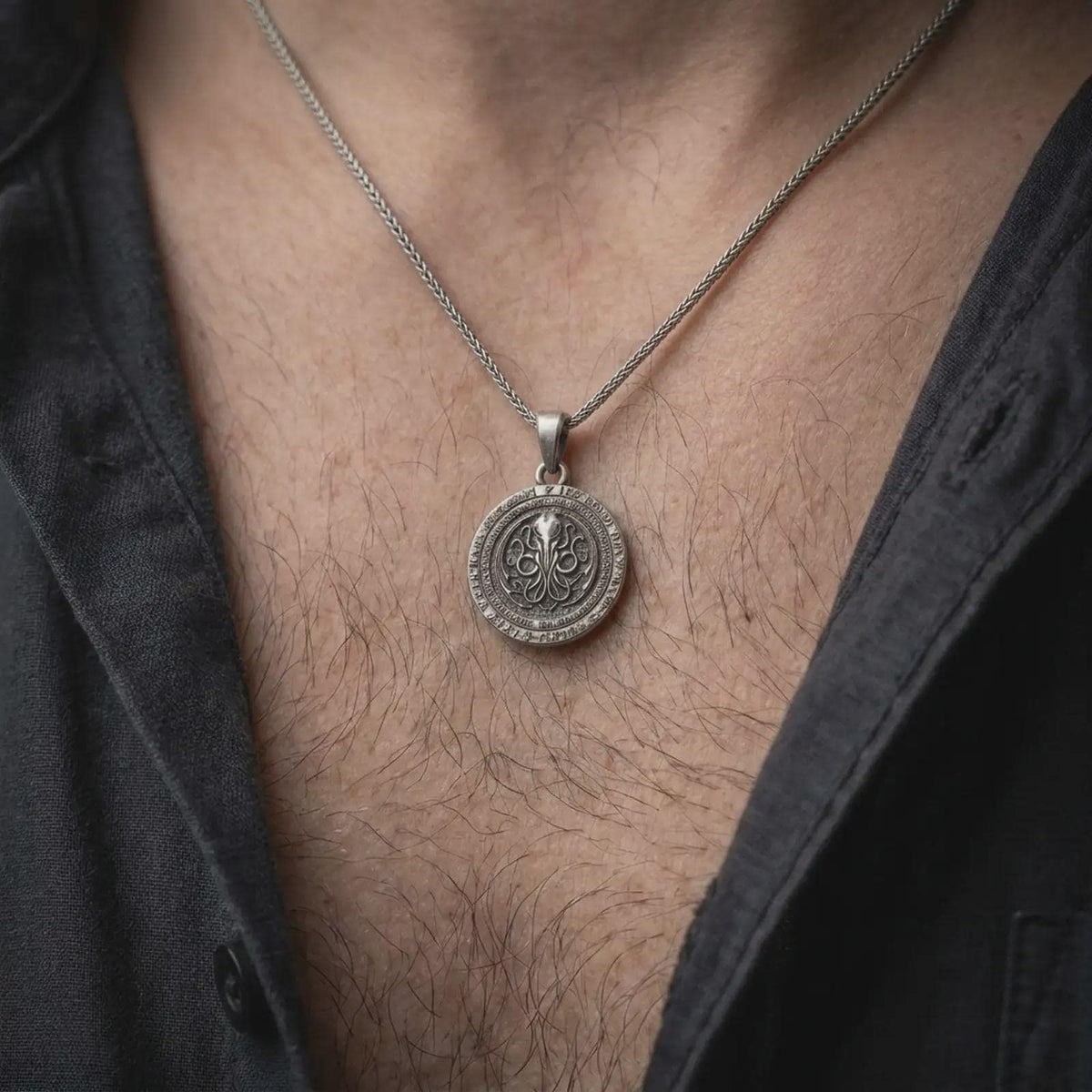 Oxidized sterling silver Cthulhu pendant worn on the chest, showing the circular horror medallion, central tentacled sigil, and engraved mythos-style outer ring details.