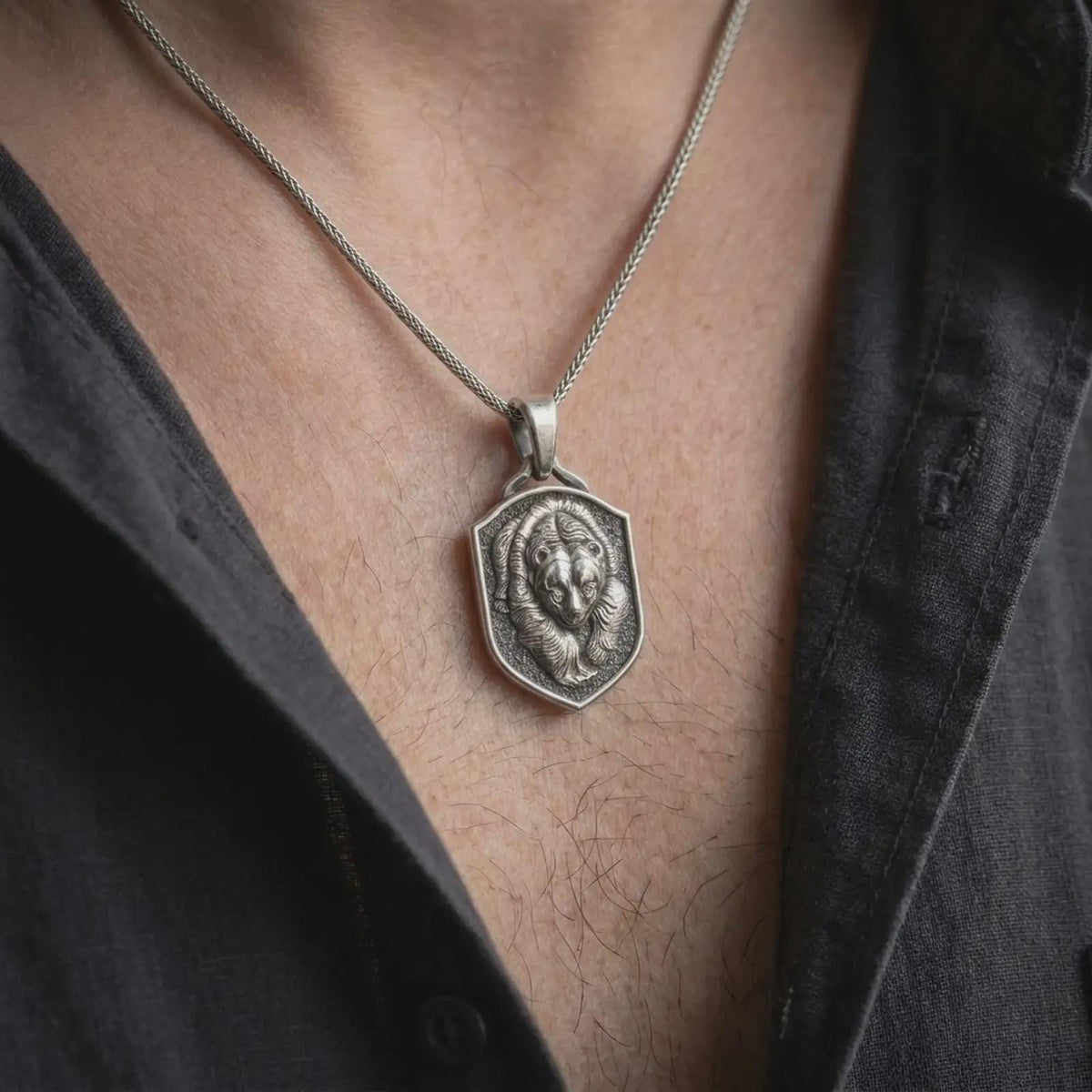 Oxidized sterling silver grizzly bear necklace worn on the chest, showing the powerful bear portrait, textured shield background, detailed fur, and rugged animal totem styling.