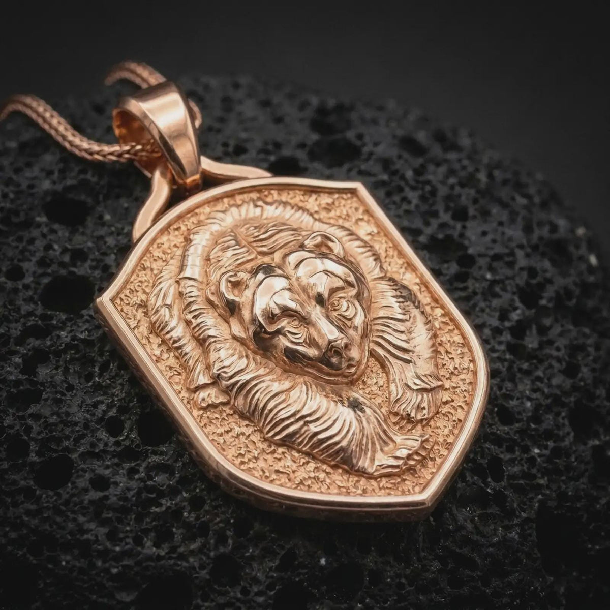 Rose gold plated bear shield necklace displayed on textured volcanic stone, showcasing the sculpted grizzly head, layered fur details, dimensional relief, and wildlife-inspired pendant design.